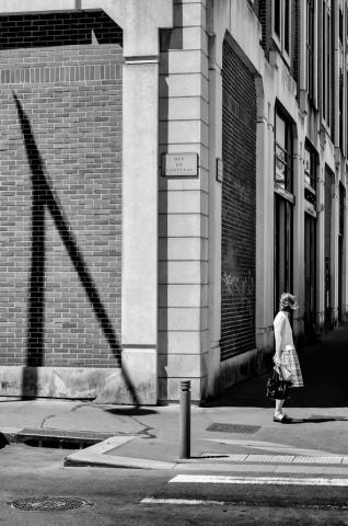 Visuel de l'exposition "Chroniques" représentant une femme en jupe se tenant sur un trottoir en ville.