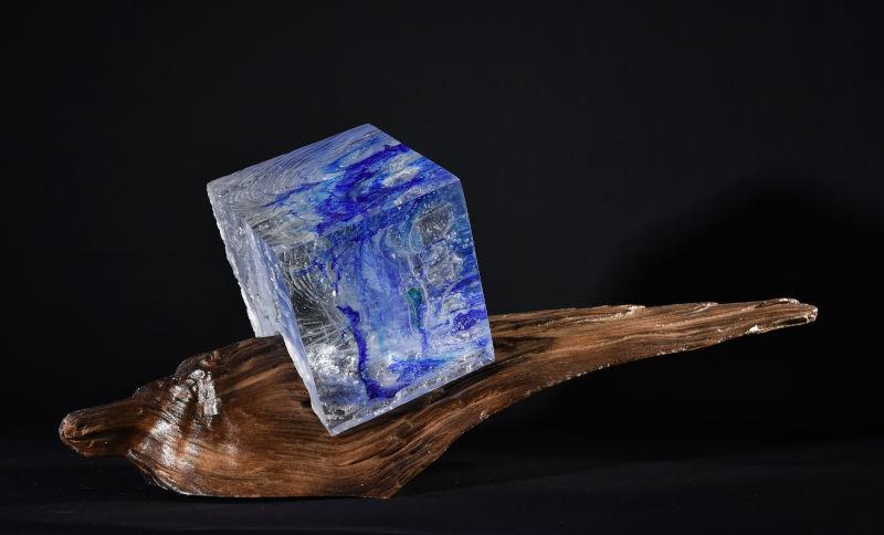 Visuel de l'exposition "Collection automne et verre", représentant un bout de bois et une pierre bleue translucide et cubique encastrés.